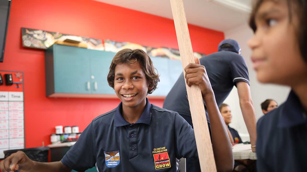 A young child smiling while holding a piece of lumber